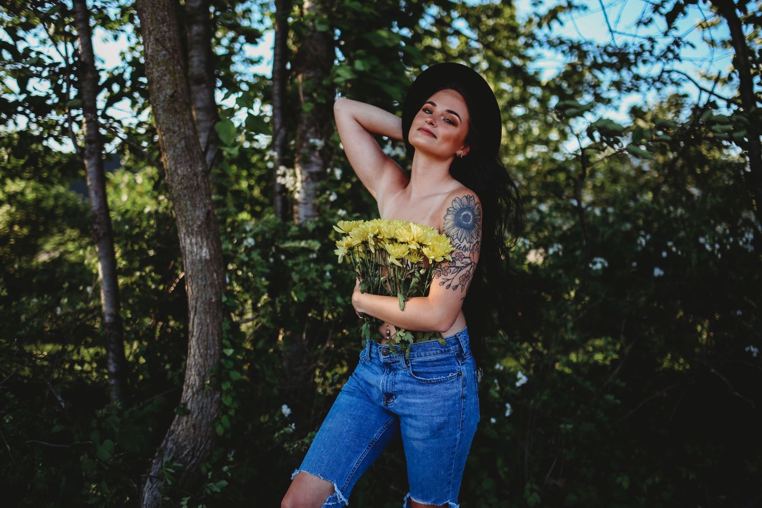 Outdoor summer portrait with blue denim against lush green trees.