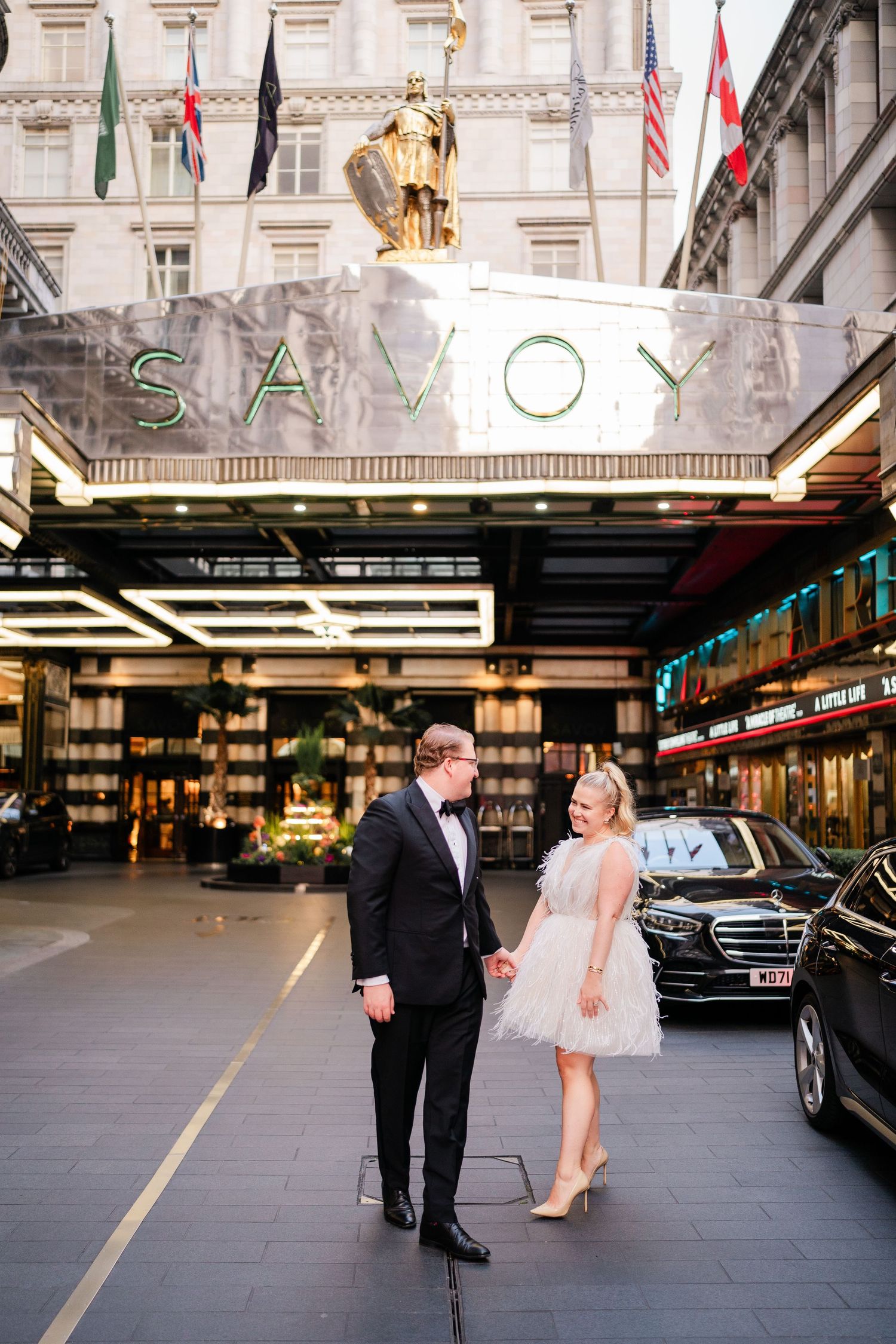 A couple poses for wedding photos outside the Savoy building in an urban setting.