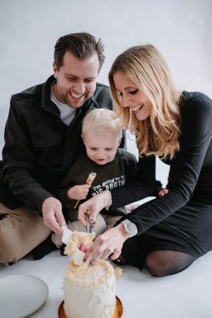 Family enjoying a cake celebration together on white backdrop.