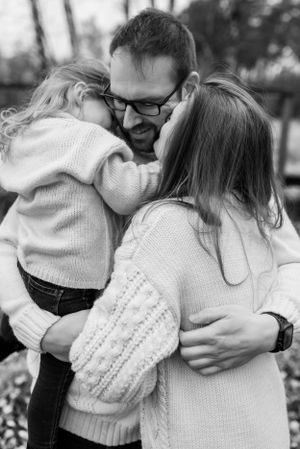 Black and white image of family sharing warm embrace outdoors in winter sweaters.