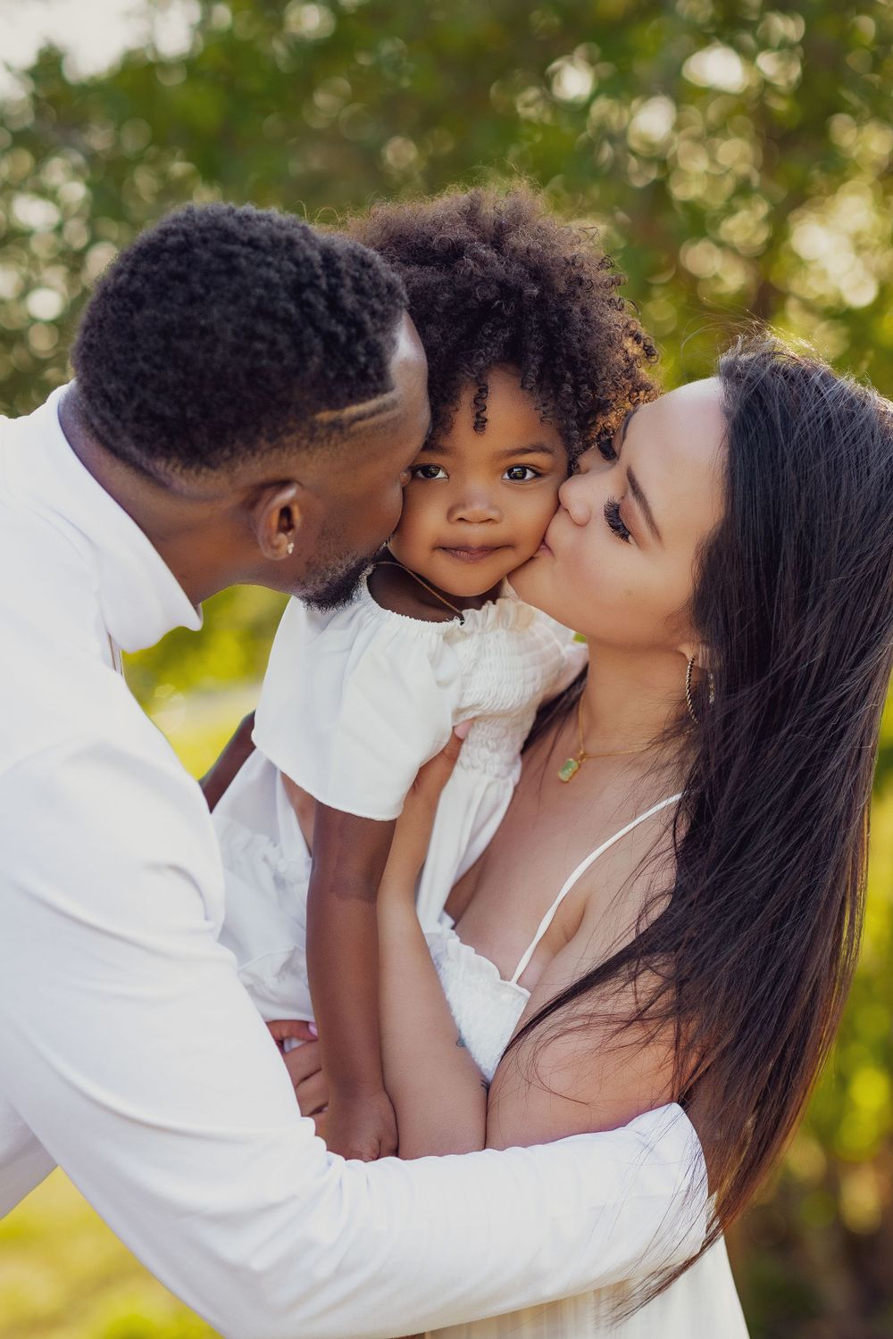 A tender family moment captured outdoors with everyone dressed in white against a natural background.