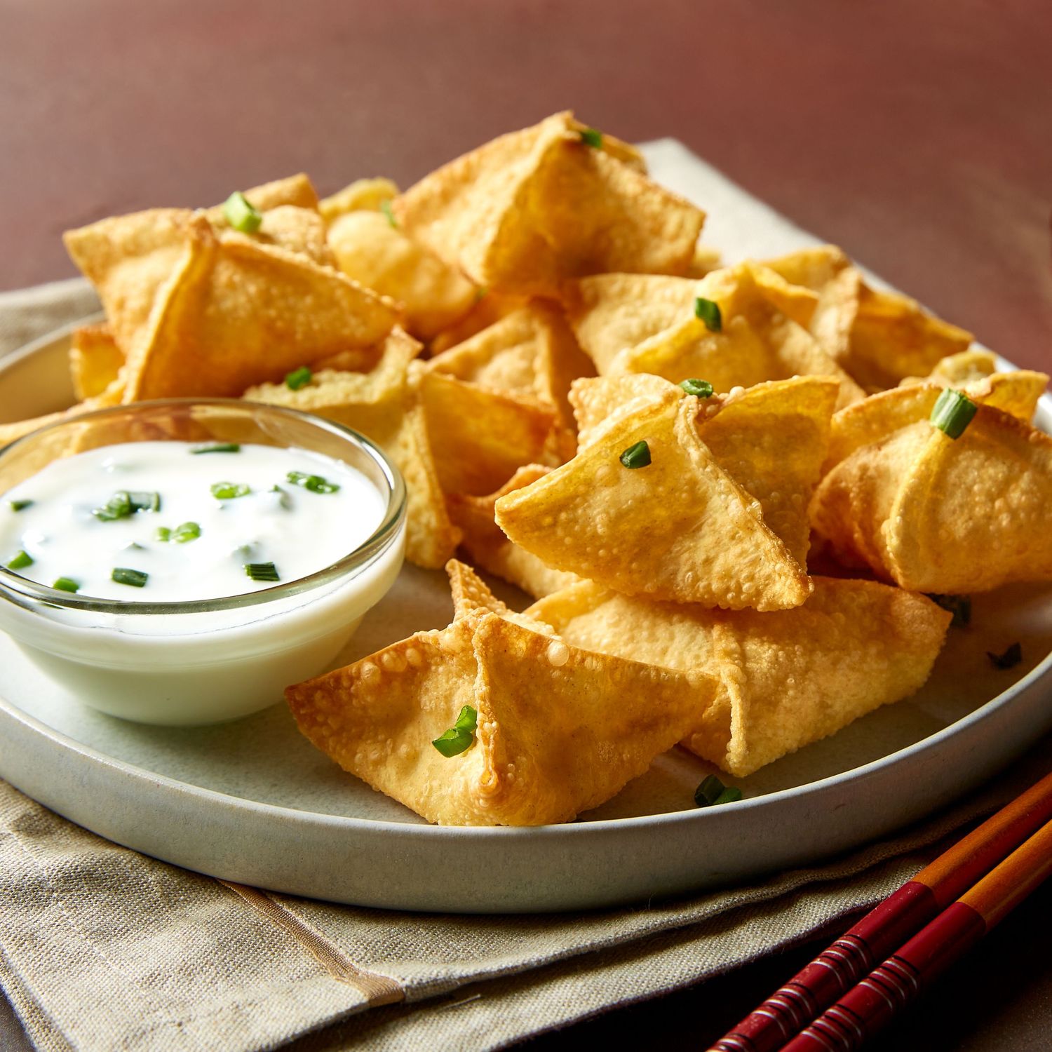 Crispy golden crab rangoon wontons served with creamy dipping sauce on textured plates against a rustic background.