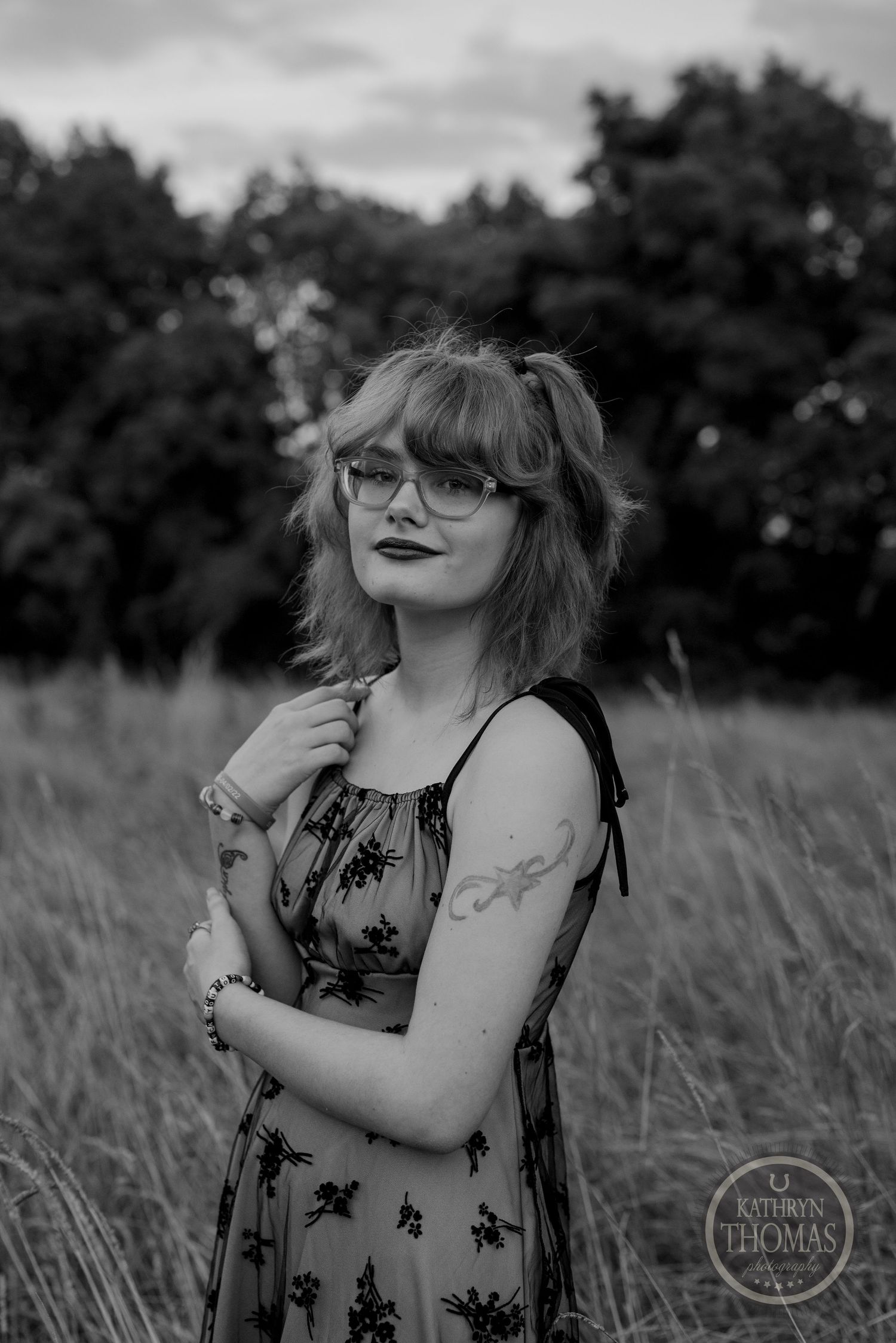 Black and white portrait in floral dress standing in tall grass field.