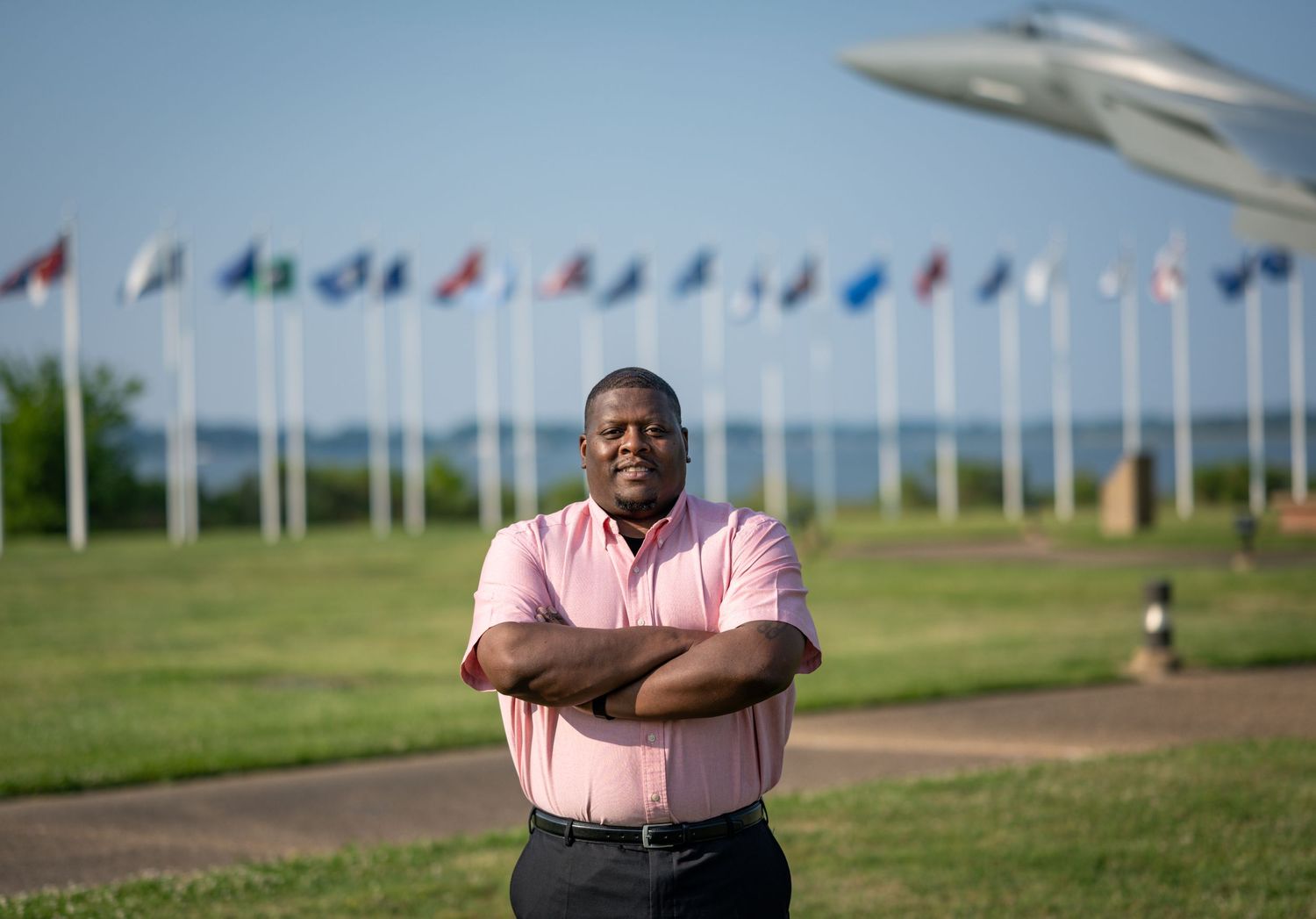 A person stands confidently in front of international flags and an aircraft display outdoors.