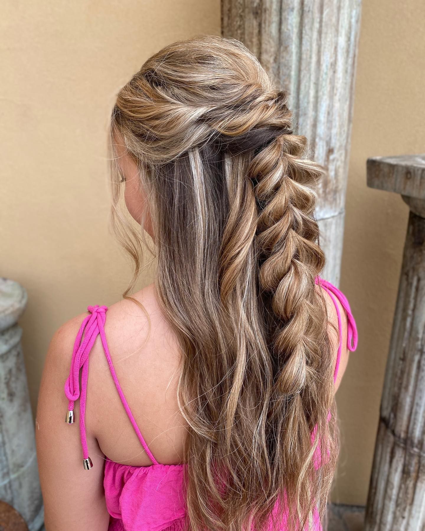 Intricate braided hairstyle with blonde highlights and half-up styling against beige background.
