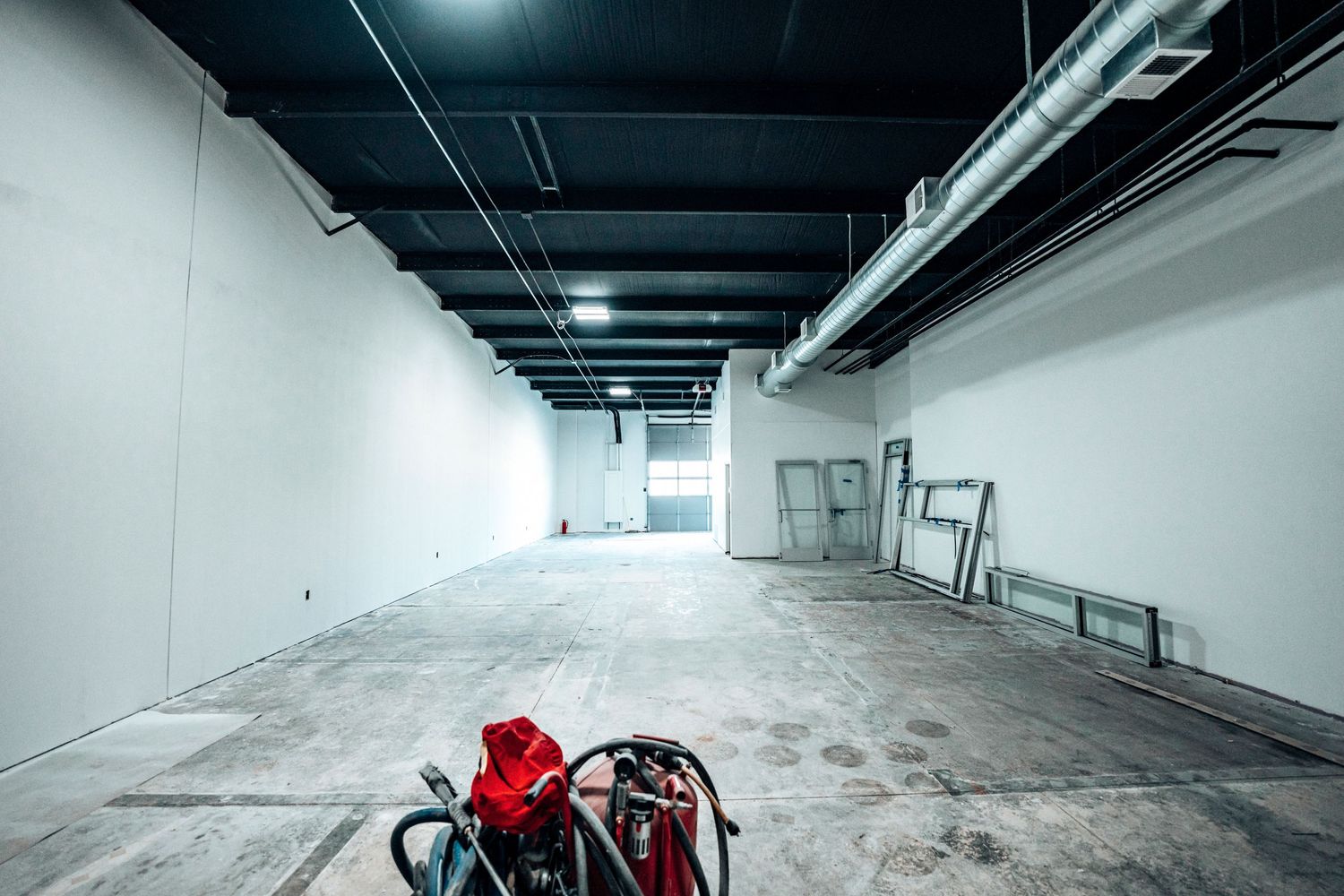 Empty industrial room with white walls features a red bag on concrete floor.