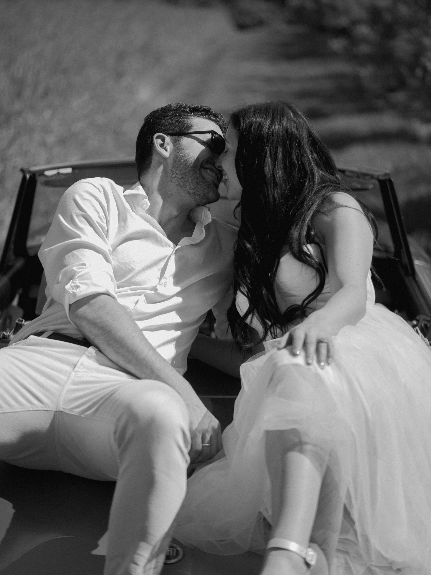 A black and white romantic photo of a couple sharing a moment in their convertible car.