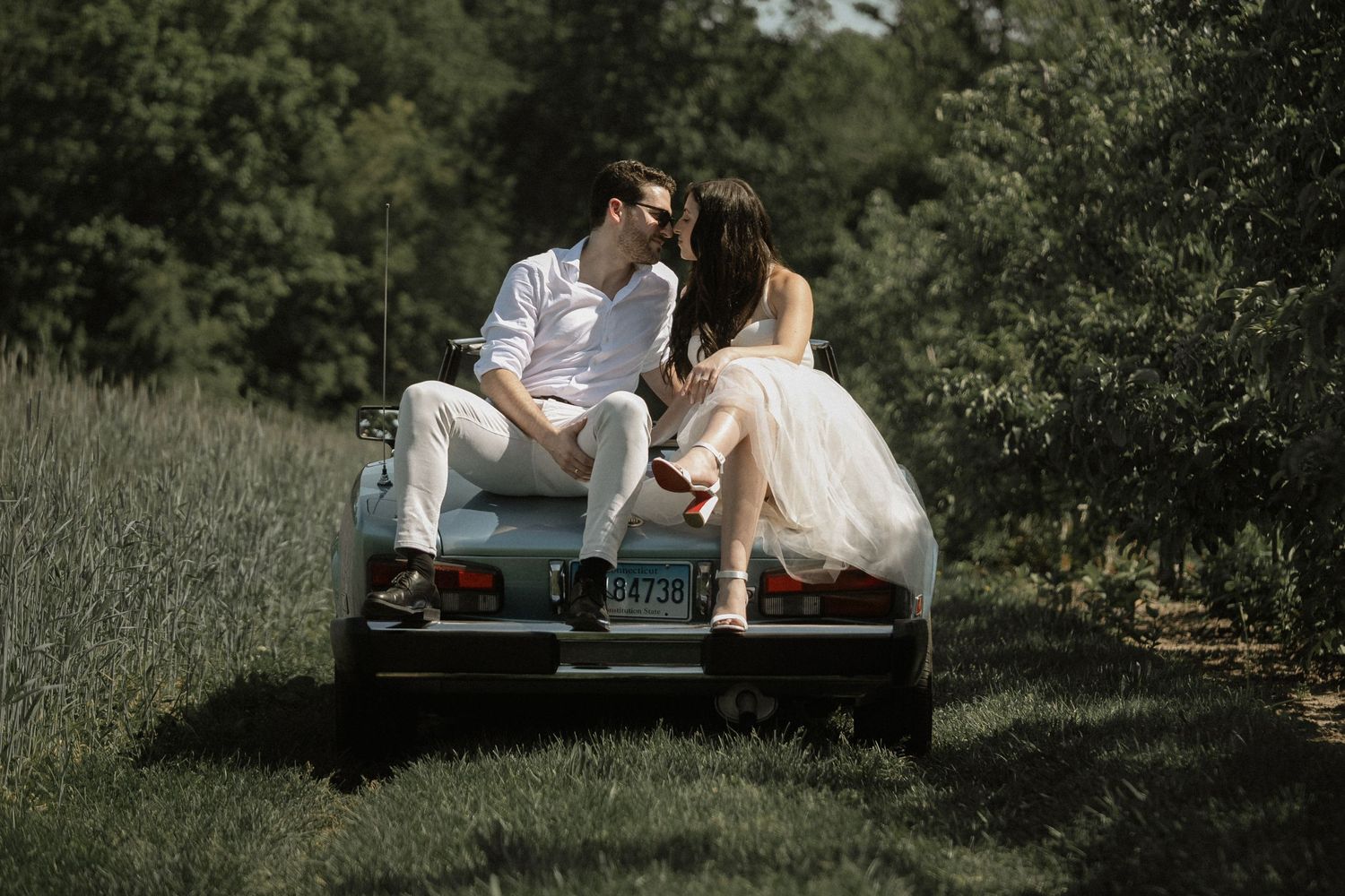 A romantic countryside photo session featuring a couple on their classic car in a meadow.