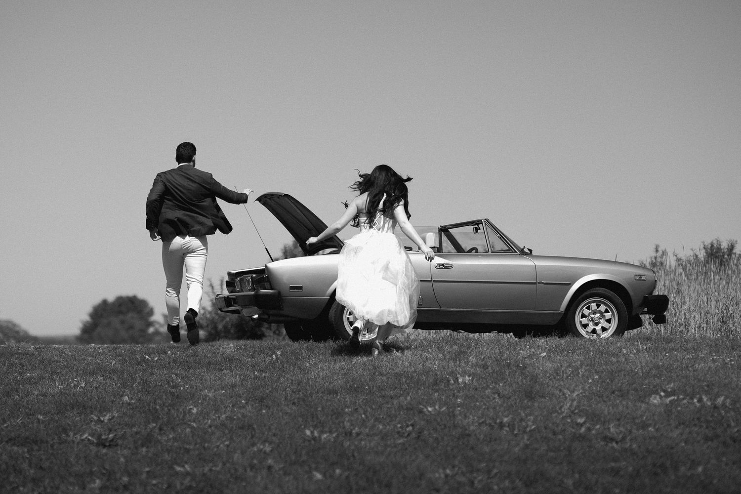 Black and white silhouette of people with a classic car in a field.