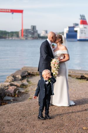 En ung pojke håller för ögonen när hans nygifta mamma och pappa kysser varann