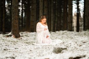 Gravid kvinna i en vit klänning i ett snöigt skogslandskap