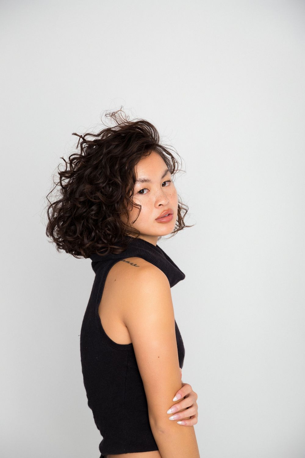 Studio portrait of woman with curly dark hair in black sleeveless top against white background.