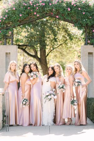 Bridal party in pink bridesmaid dresses posed under a floral arch.
