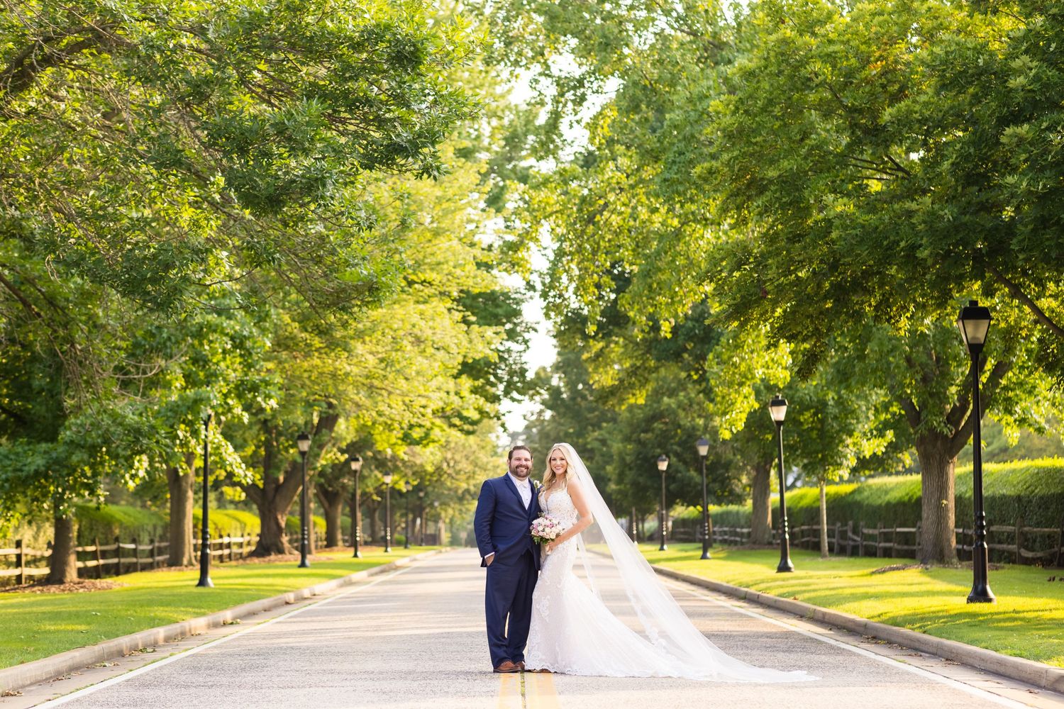 A couple stands on a tree-lined path during their wedding photoshoot.