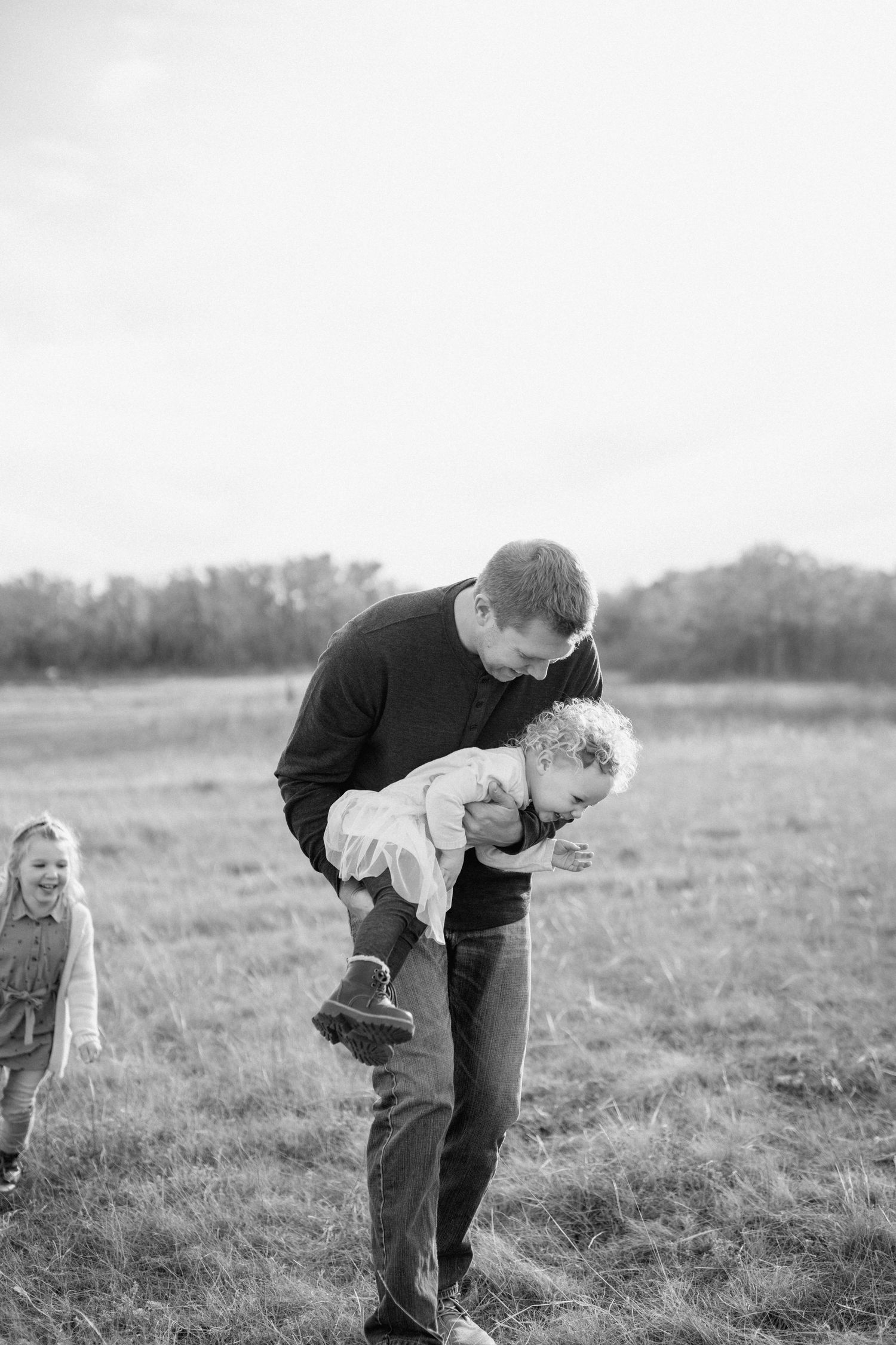 Black and white photo of family playtime in a field during golden hour.