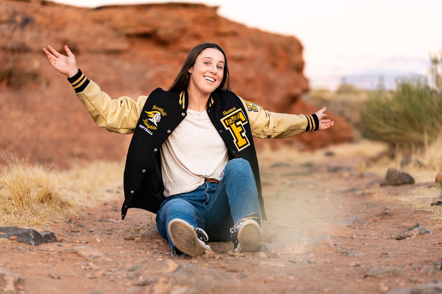 girl-sitting-n-red-dirt-red-rocks-in=letterman's-jacket-for-senior-photos