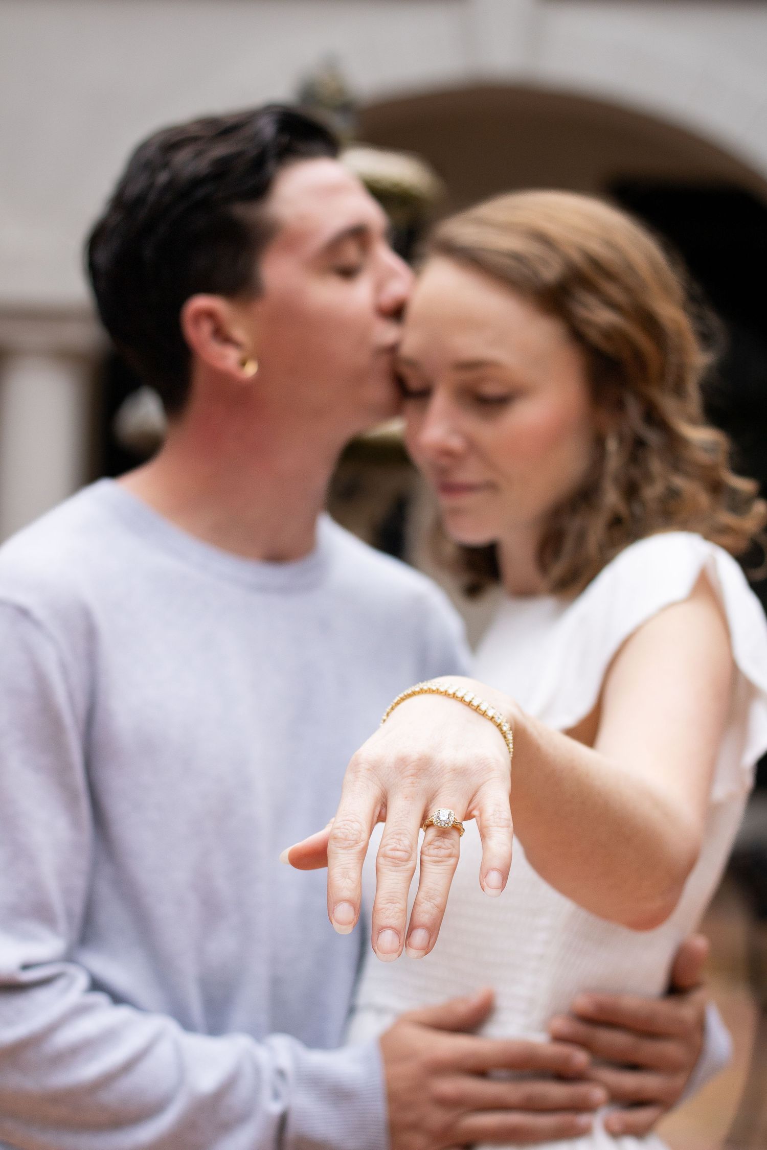 A couple shares a tender moment while showing off an engagement ring.