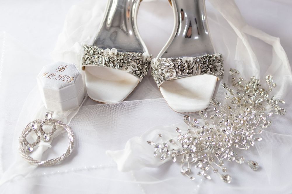 Bridal accessories including white heels, jewelry and crystal hair piece on white fabric.