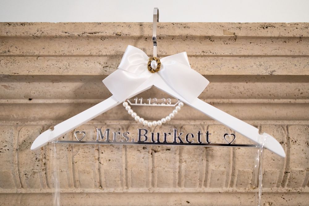 A personalized white wedding dress hanger with 'Mrs. Burkert' text against a textured wall.