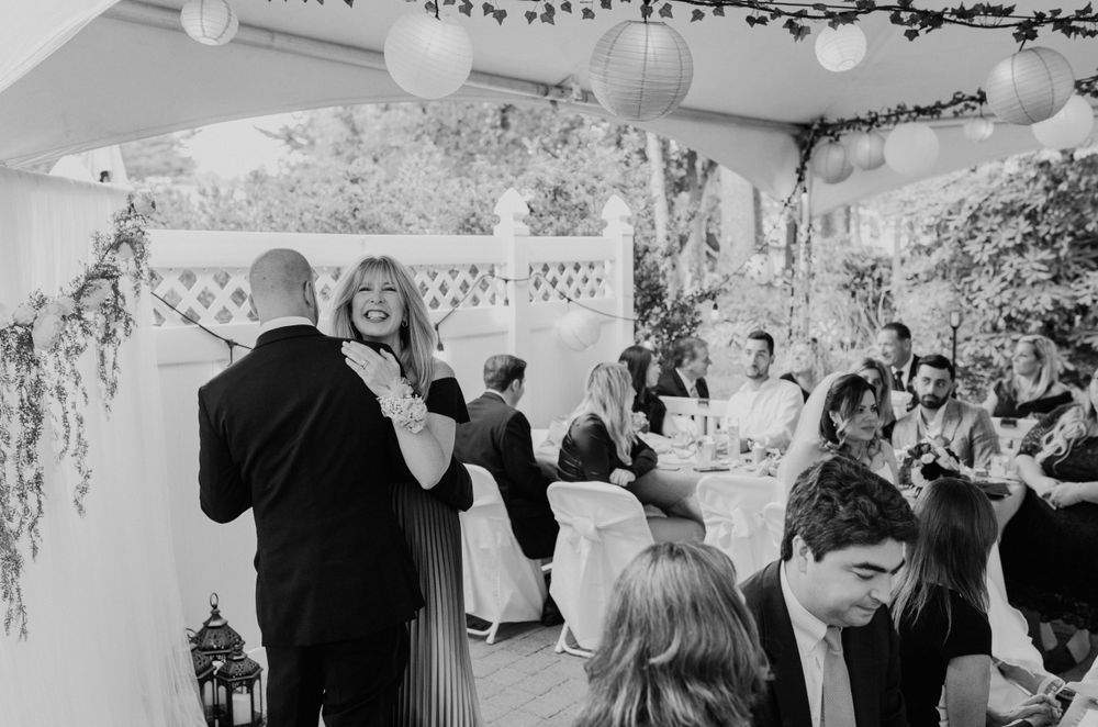 Black and white photo of couples dancing at an indoor wedding reception with decorative greenery.