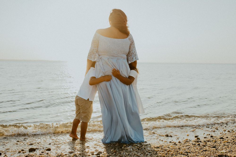 Parent and child in matching light clothing walking along shoreline at sunset.