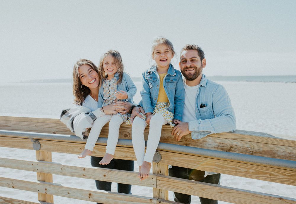 A family sitting together on a wooden pier overlooking the ocean.