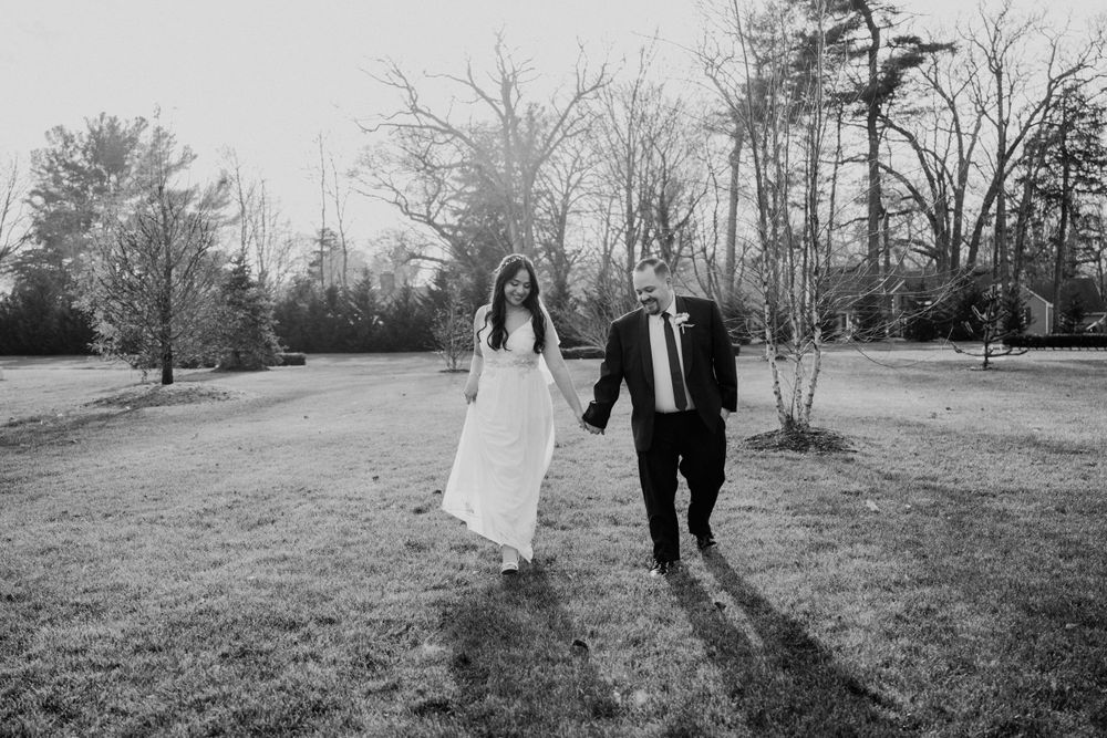 A black and white photo of newlyweds running together through an outdoor garden setting.
