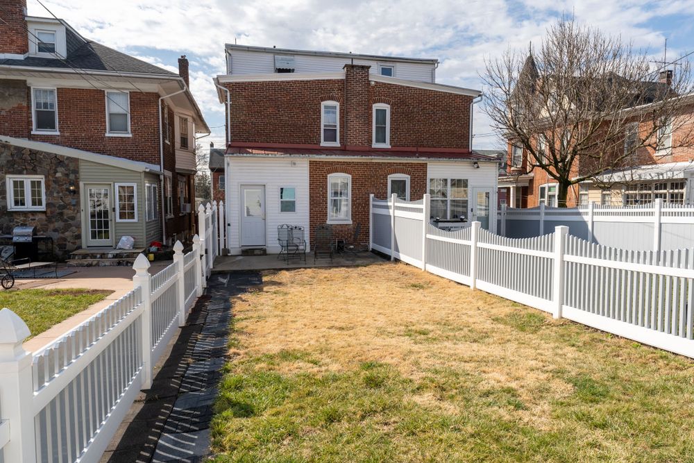Fenced backyard with brown grass between brick row houses.
