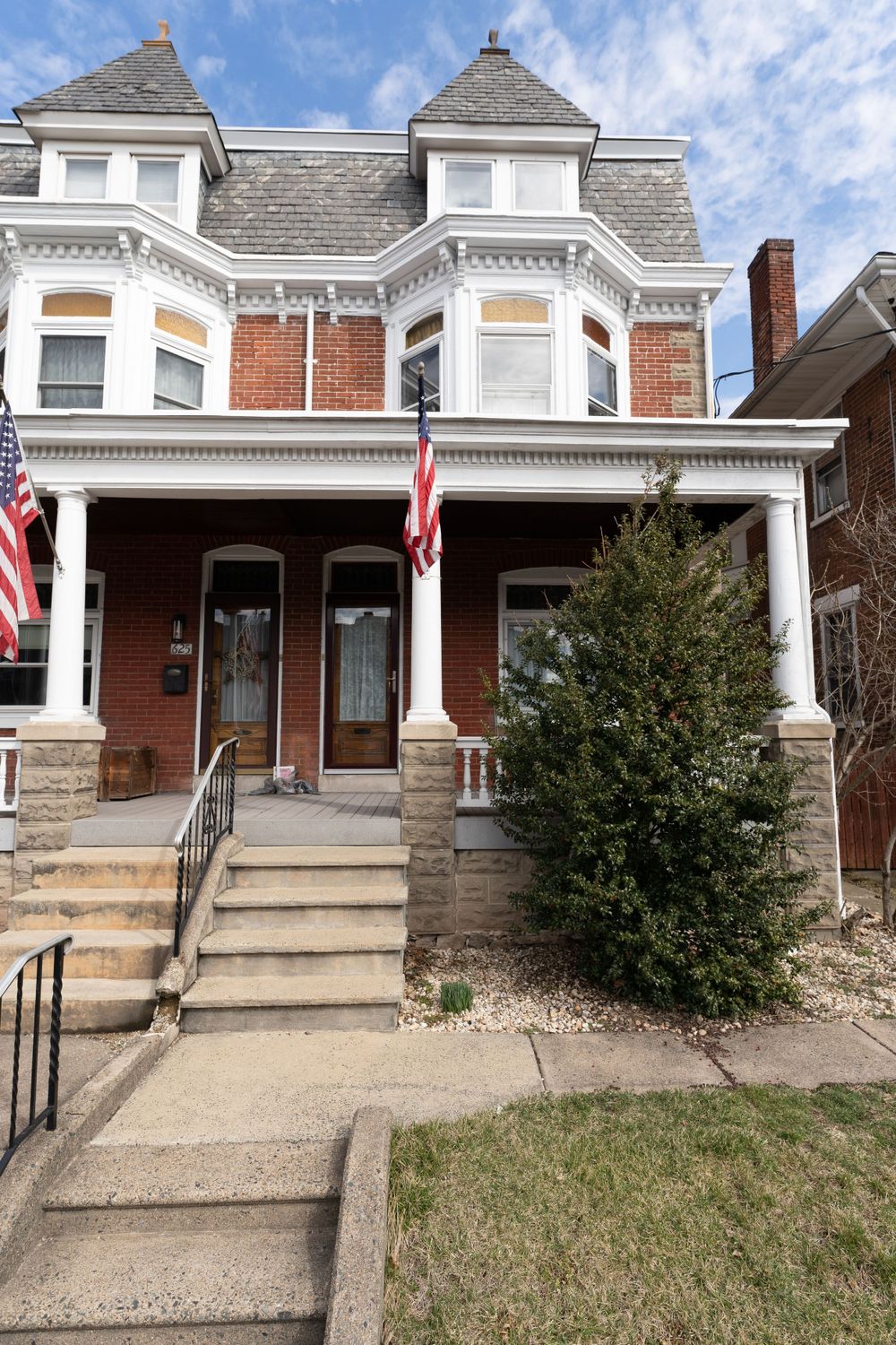 Victorian-style duplex with mansard roof, brick facade, and American flags.