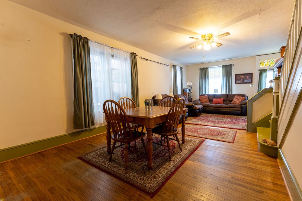 Dining room with hardwood floors, traditional wooden furniture, and brown leather sofa in background.