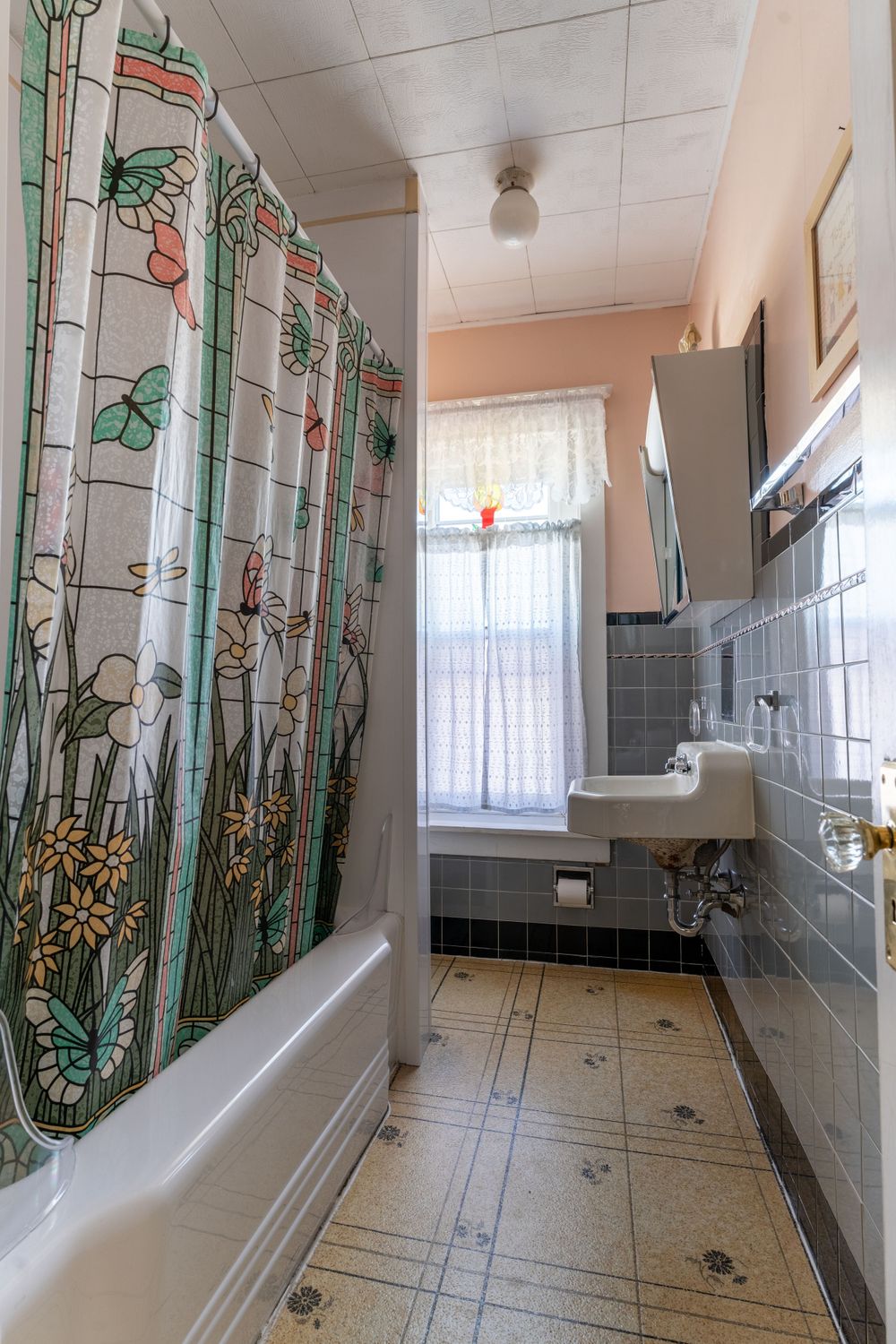 Vintage bathroom with decorative floral shower curtain, blue tile walls, and white fixtures.