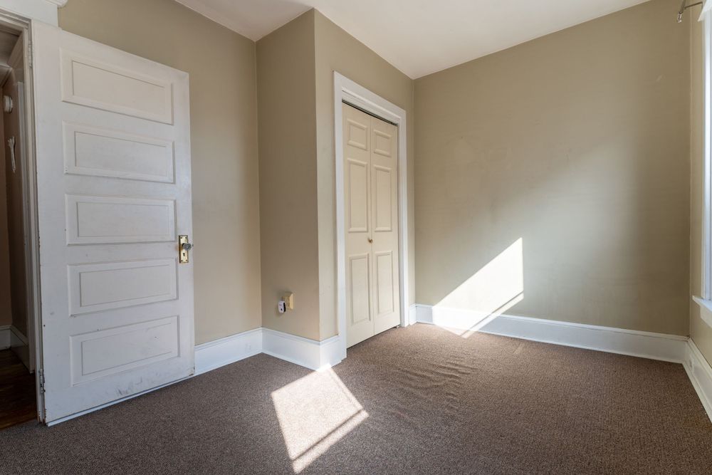 Empty room with beige walls, white trim, and sunlight streaming through door.