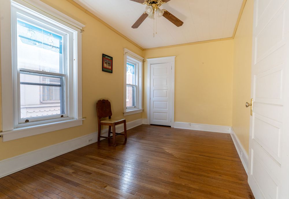 Bright yellow bedroom with hardwood floors, ceiling fan, and white trim details.