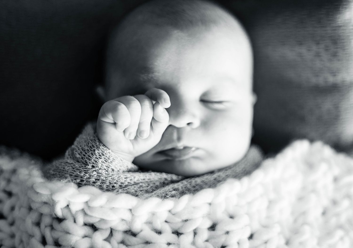 Peaceful black and white image of sleeping newborn with hand near face.