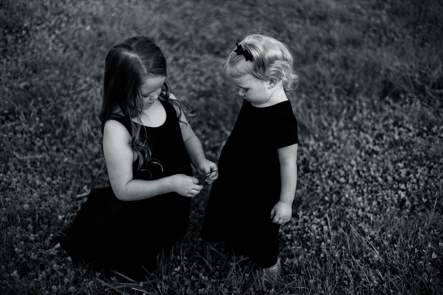 Black and white photo of two people in black dresses on grass.