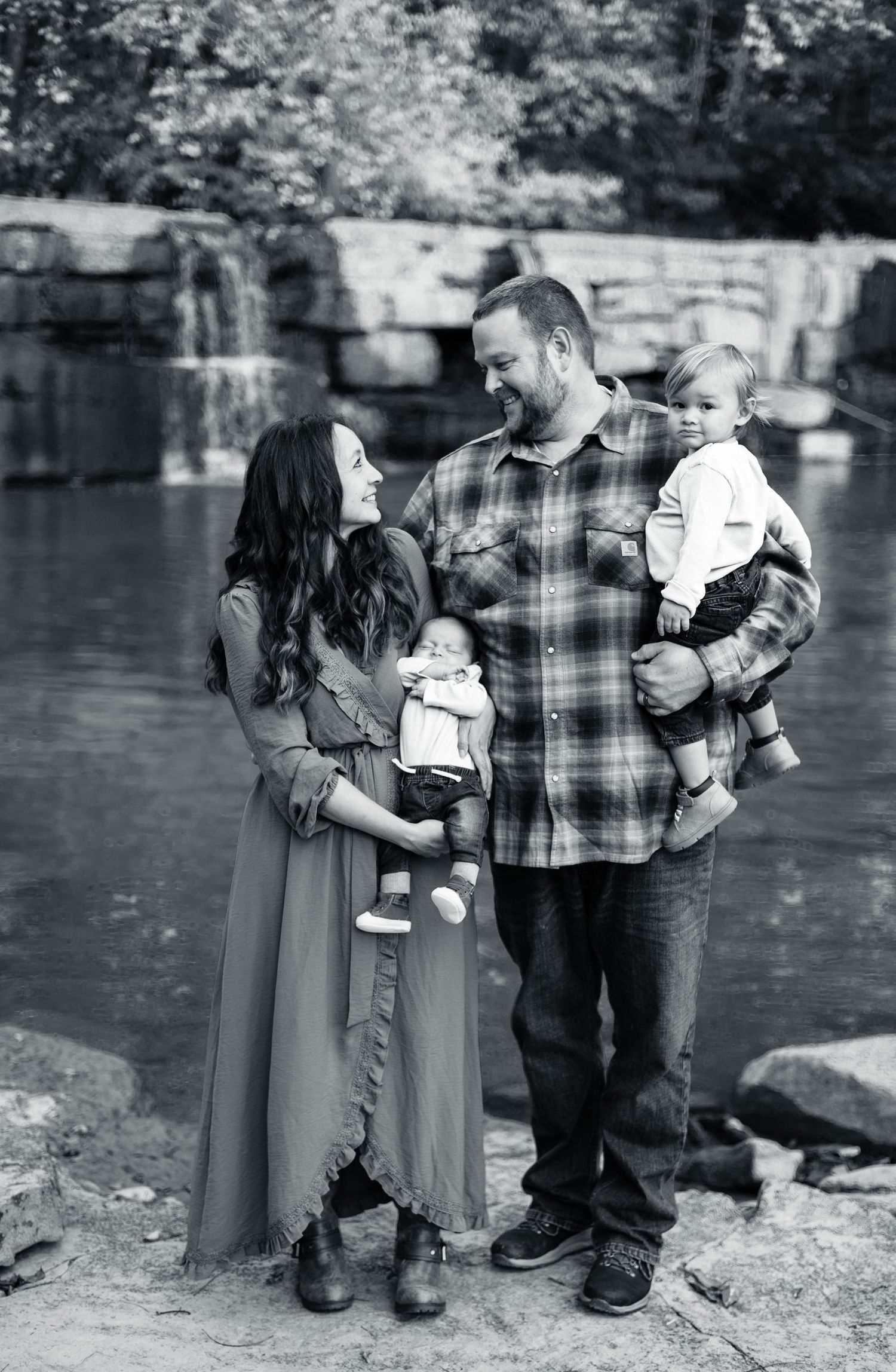Black and white family portrait by a waterfall with parents holding children.