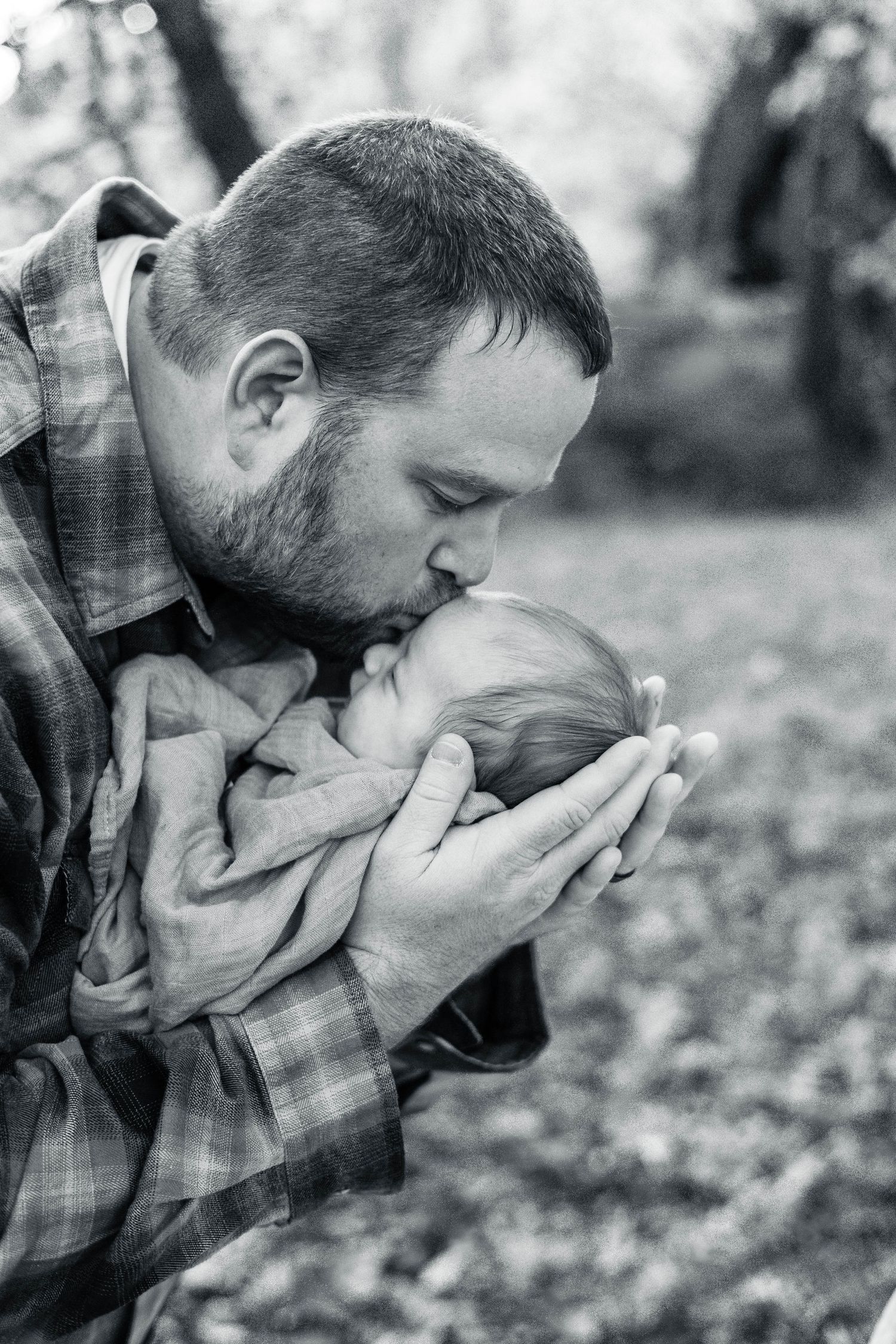 An intimate black and white moment of parent giving baby a gentle kiss on the head.