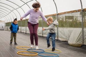 Therapist jumping through hoops with a child in a polytunnel.