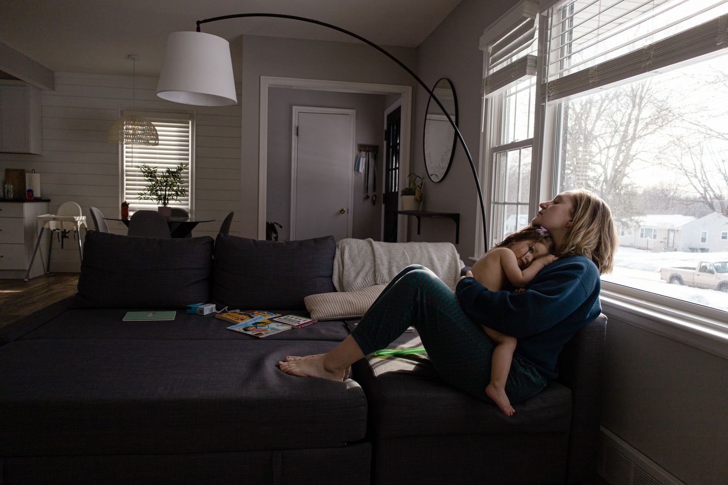 Sioux City, Iowa photographer. Mother holding toddler on couch by window in cozy living room during winter.