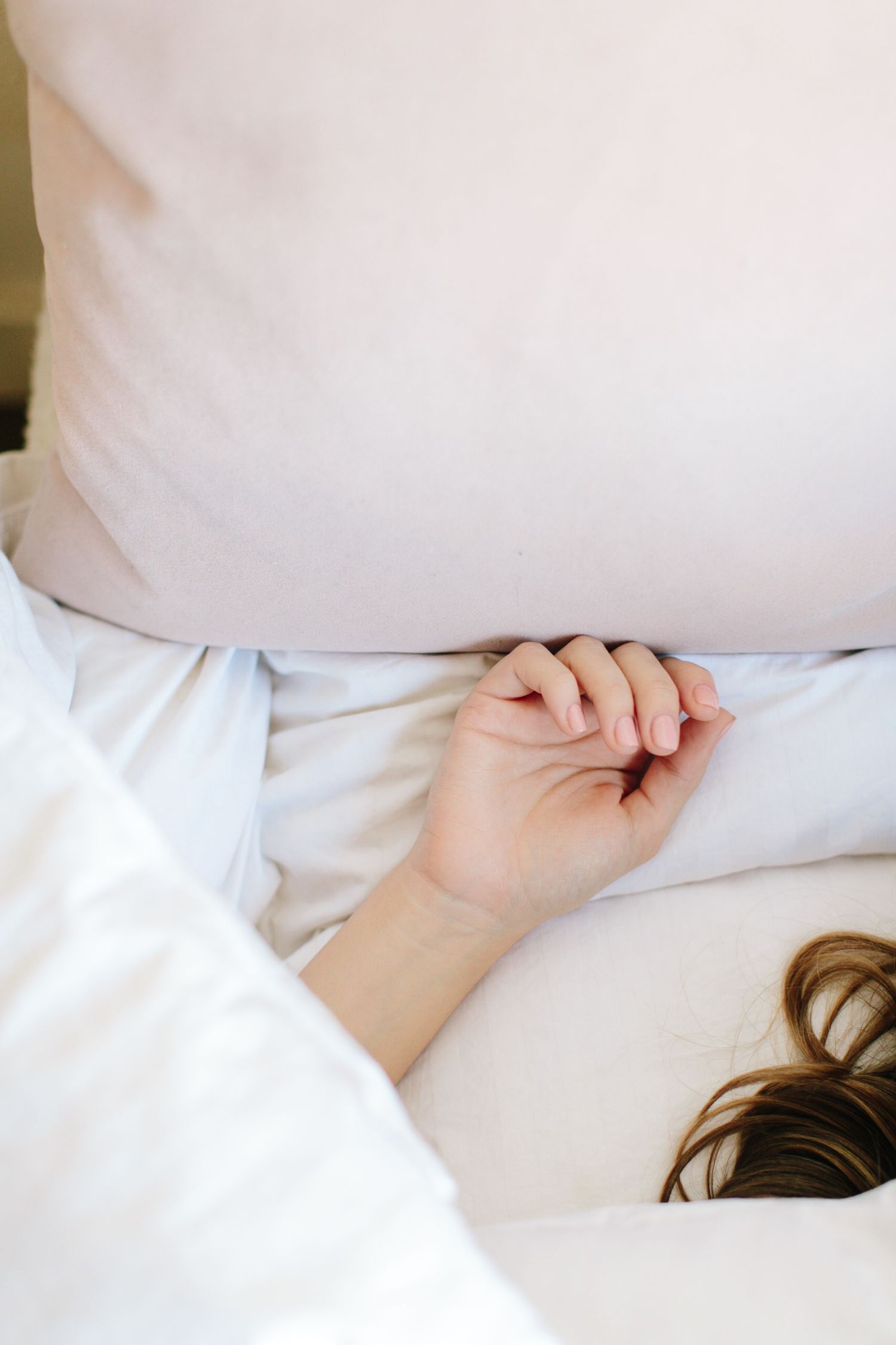 Close-up of hand resting on white pillow and bedding in soft morning light.