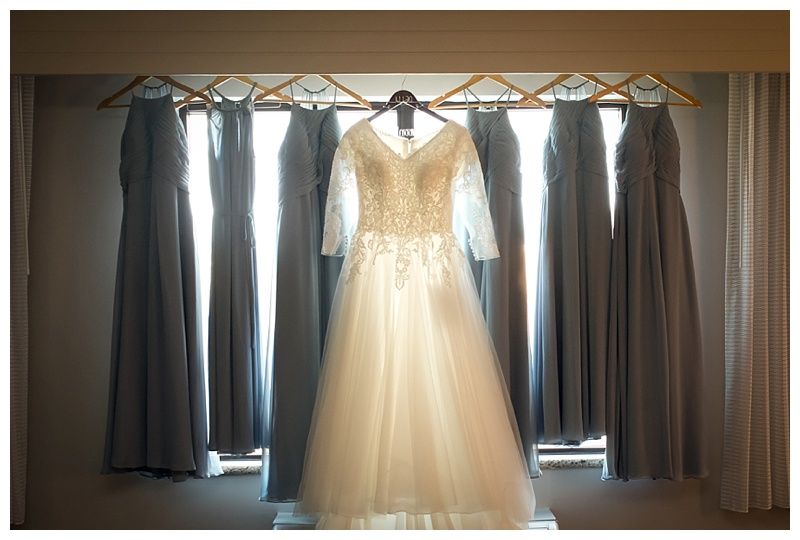 Wedding dress hanging in natural window light with bridesmaids dresses.