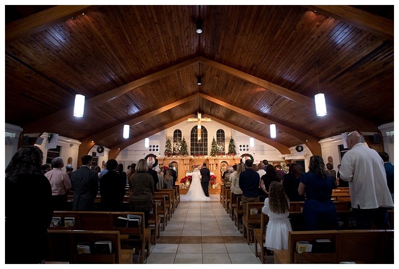 Panoramic view of a church interior with vaulted wooden ceiling and altar during a wedding ceremony.