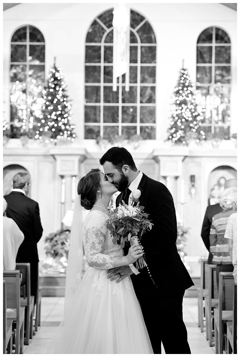 A romantic wedding ceremony in a chapel with arched windows and Christmas trees decorating the altar.