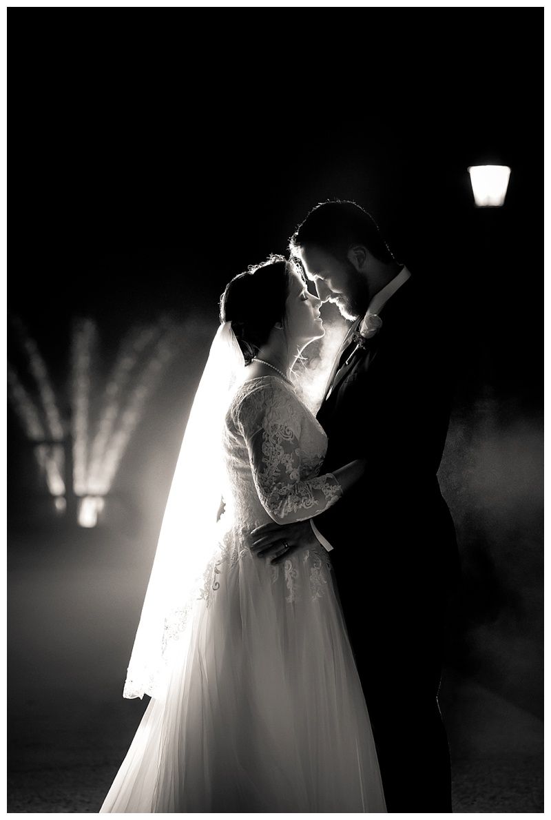 A dramatic backlit silhouette of a couple in wedding attire sharing an intimate moment.