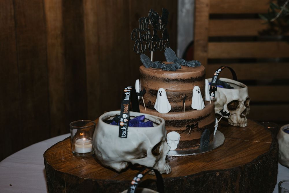 gothic wedding cake with ghosts and skulls on a wooden table at Pangdean barn for a Halloween Wedding