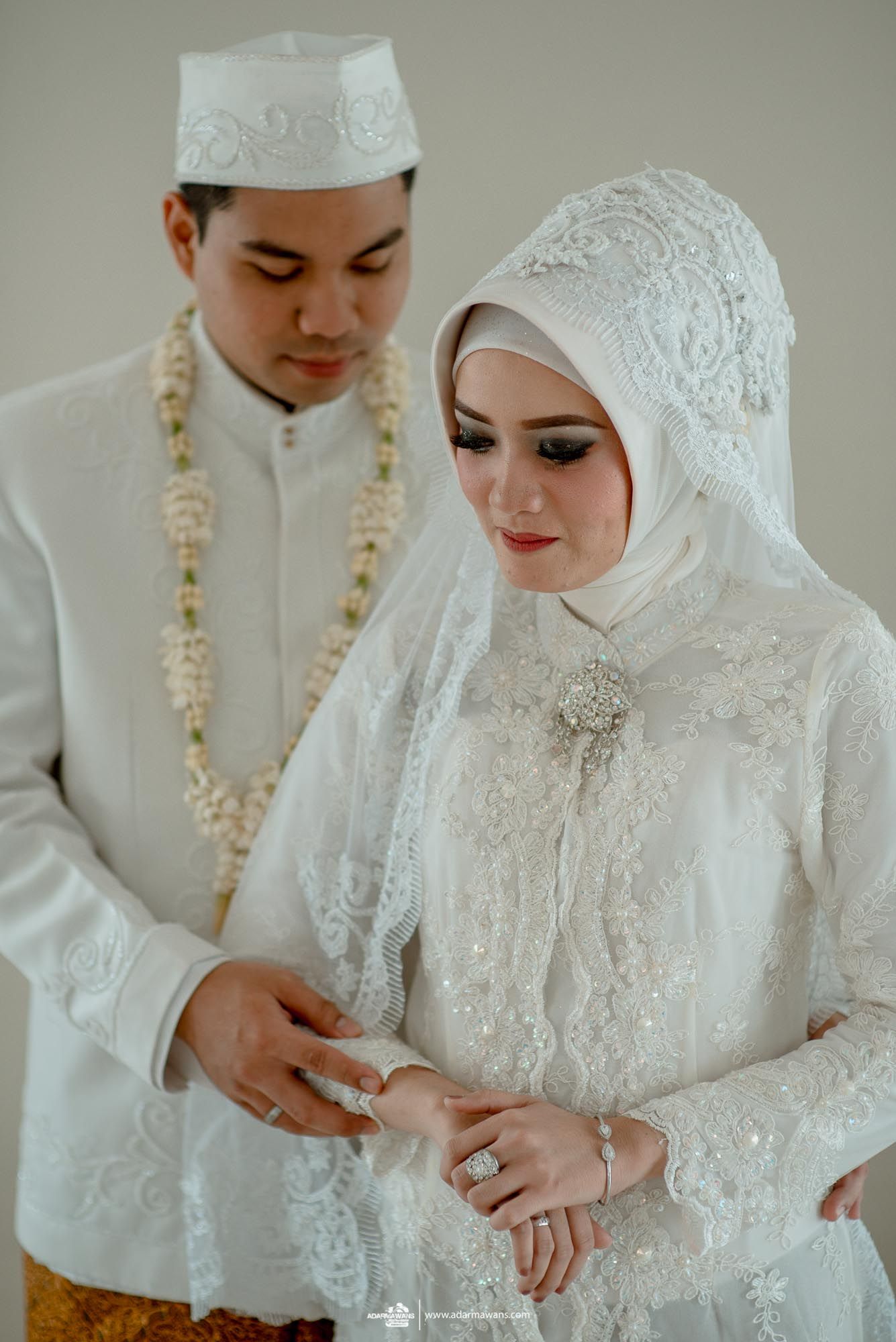 Wedding couple in white traditional Indonesian formal attire exchanging rings.