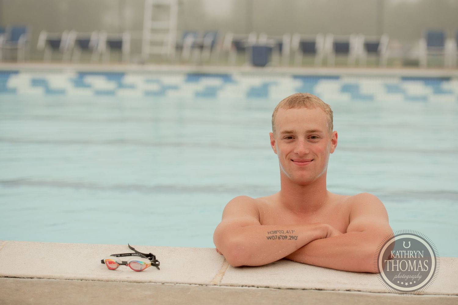 A swimmer rests on the edge of a pool with arms crossed and swim goggles nearby.