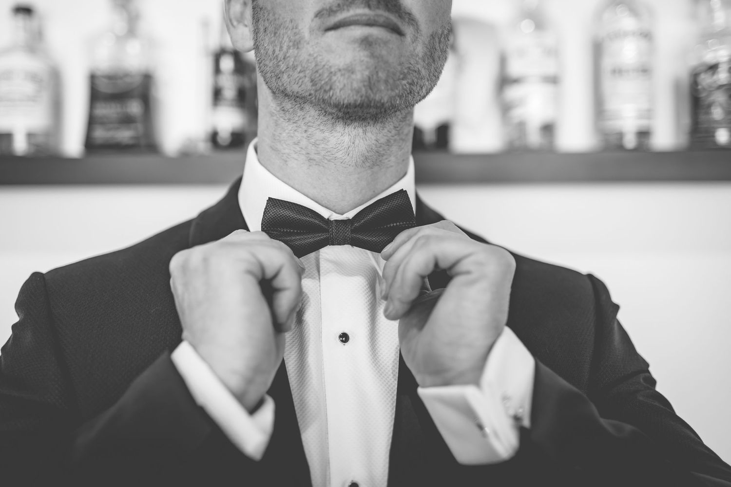 Close-up view of someone adjusting a formal black bow tie with tuxedo and white dress shirt.