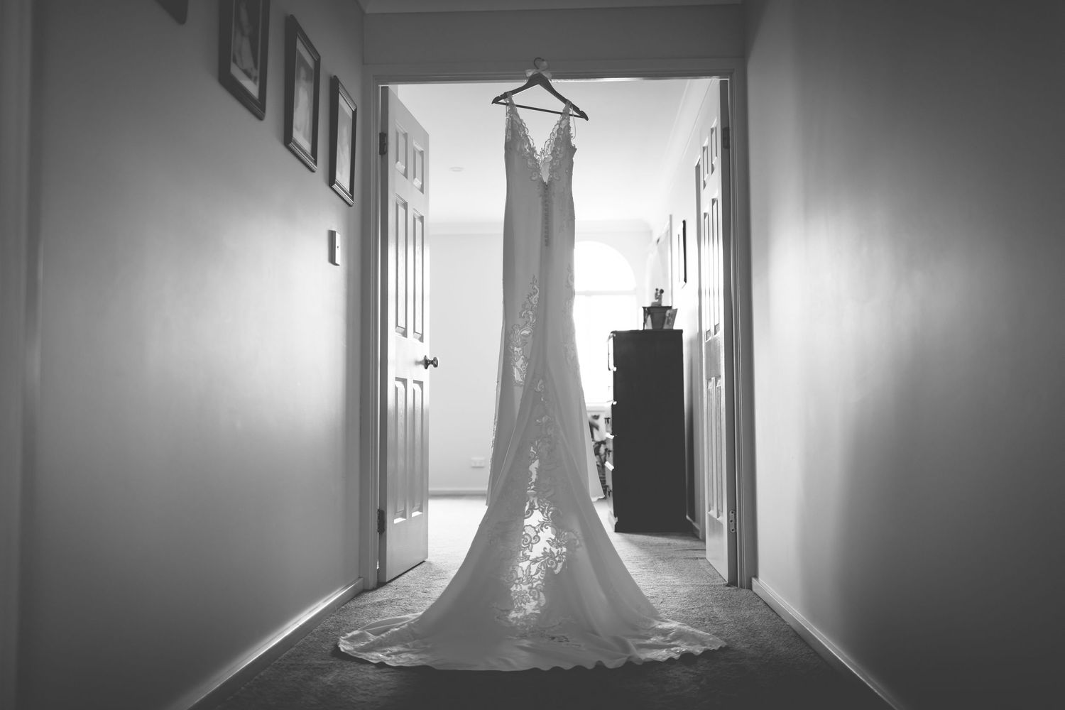 Dramatic black and white photo of wedding gown silhouetted in hallway.