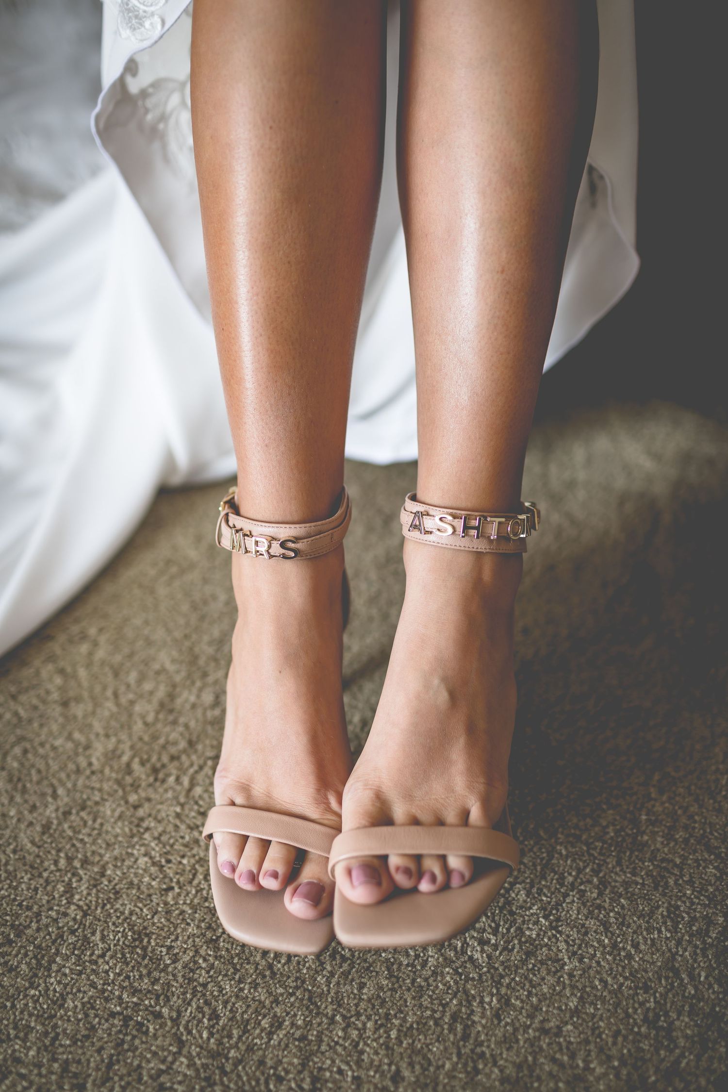 Close-up of nude wedding sandals with crystal details on beige carpet.